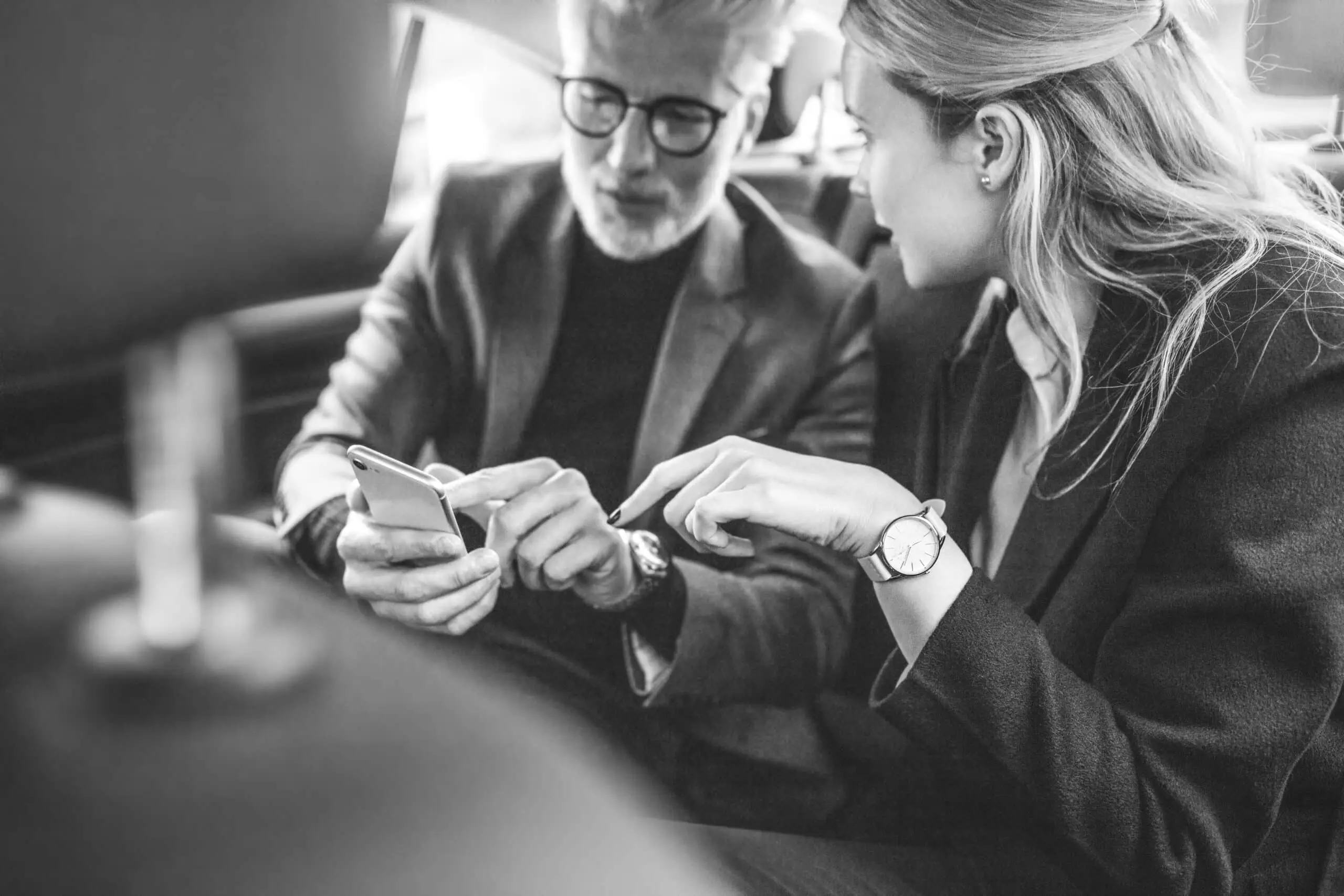 Young woman with senior businessman using mobile phone while traveling by a car. Business people using smart phone in taxi.