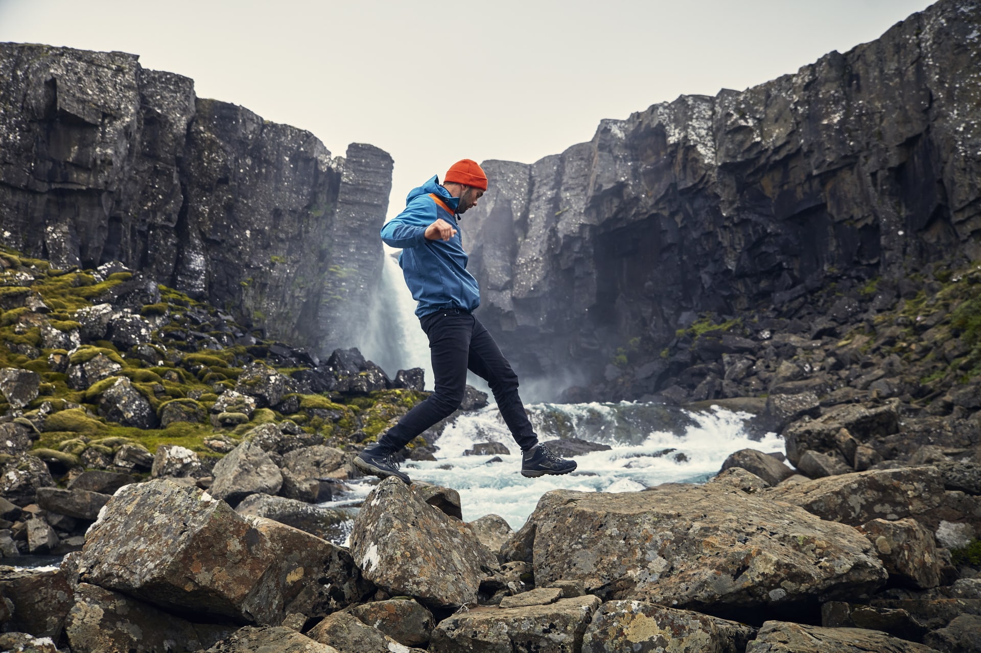 Young man crossing the stream. Jumping on rocks