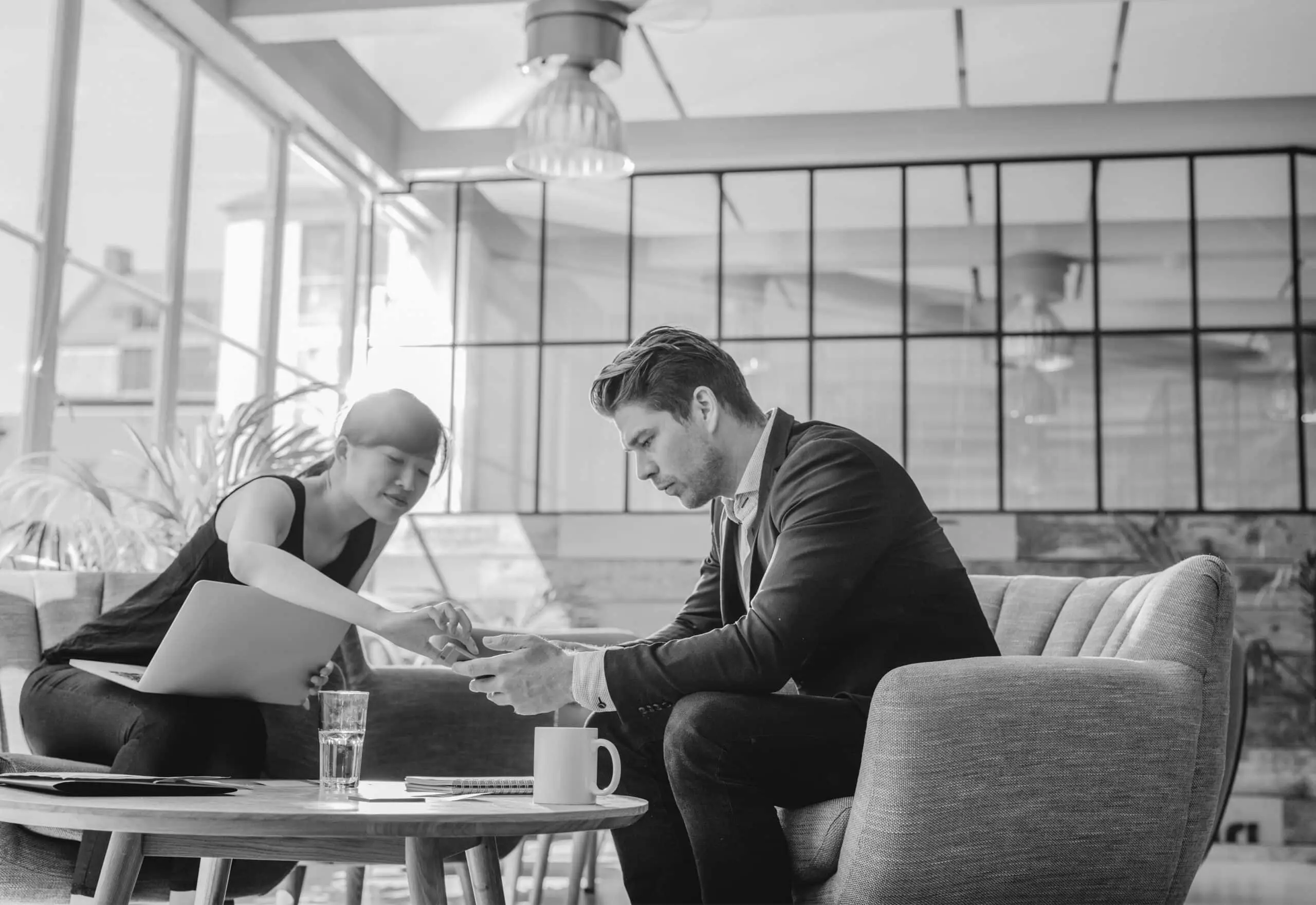 Shot of two people sitting in office lobby. Business partners working together in modern office looking at mobile phone.